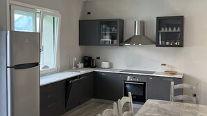 Une cuisine moderne avec des meubles gris, un réfrigérateur en acier inoxydable, un lave-vaisselle et une table à manger avec des chaises.
