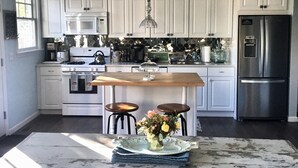 A modern kitchen with white cabinets, a stainless steel refrigerator, a chandelier, and a central island with stools.