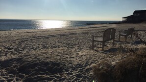 A beach with a wooden bench and a house in the background.