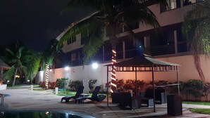 A nighttime outdoor area with lounge chairs, a pool, and a building with illuminated stripes. - Yikal house. Beautiful house 4 rooms (10 pers), 4 tennis court pools. (38)
