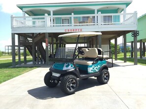 A golf cart parked in front of a building with a balcony and the name 'CHONPYS' visible. - Chompy's Beach Cabin (Bolivar Peninsula)