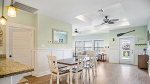 Un coin repas avec une table et des chaises en bois, un ventilateur de plafond et une vue sur l’extérieur par une porte.