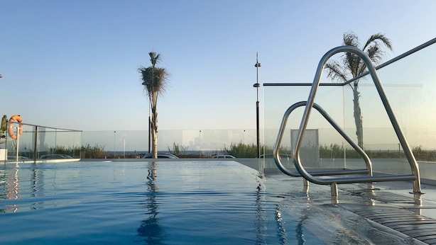 A swimming pool with clear water, metal railings, and palm trees in the background. - The Buddha House Torrox Costa (Torrox Costa)