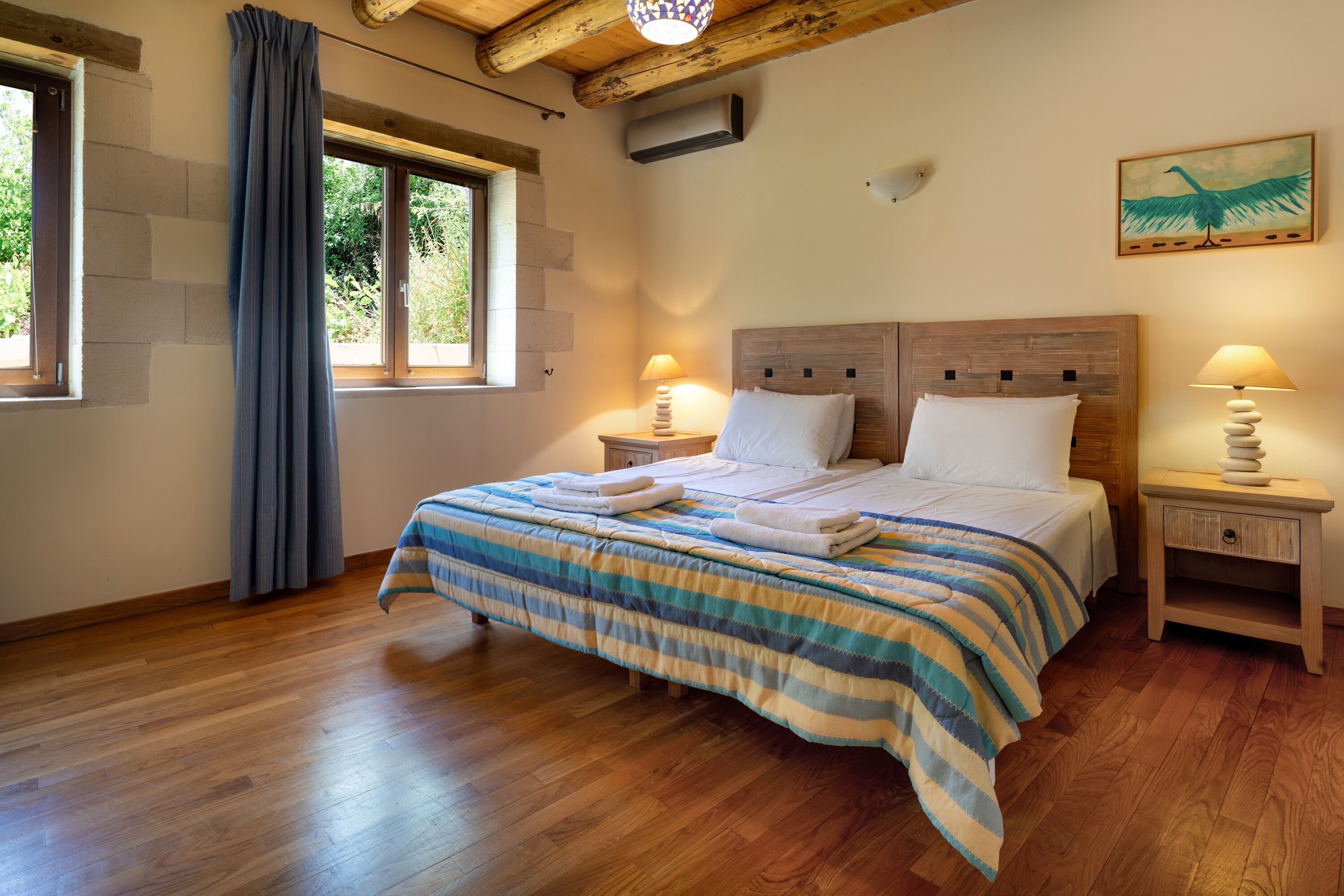 Un lit bien fait, recouvert d’une couvre-lit à rayures, deux tables de chevet avec des lampes, une tête de lit en bois et une fenêtre avec des rideaux.