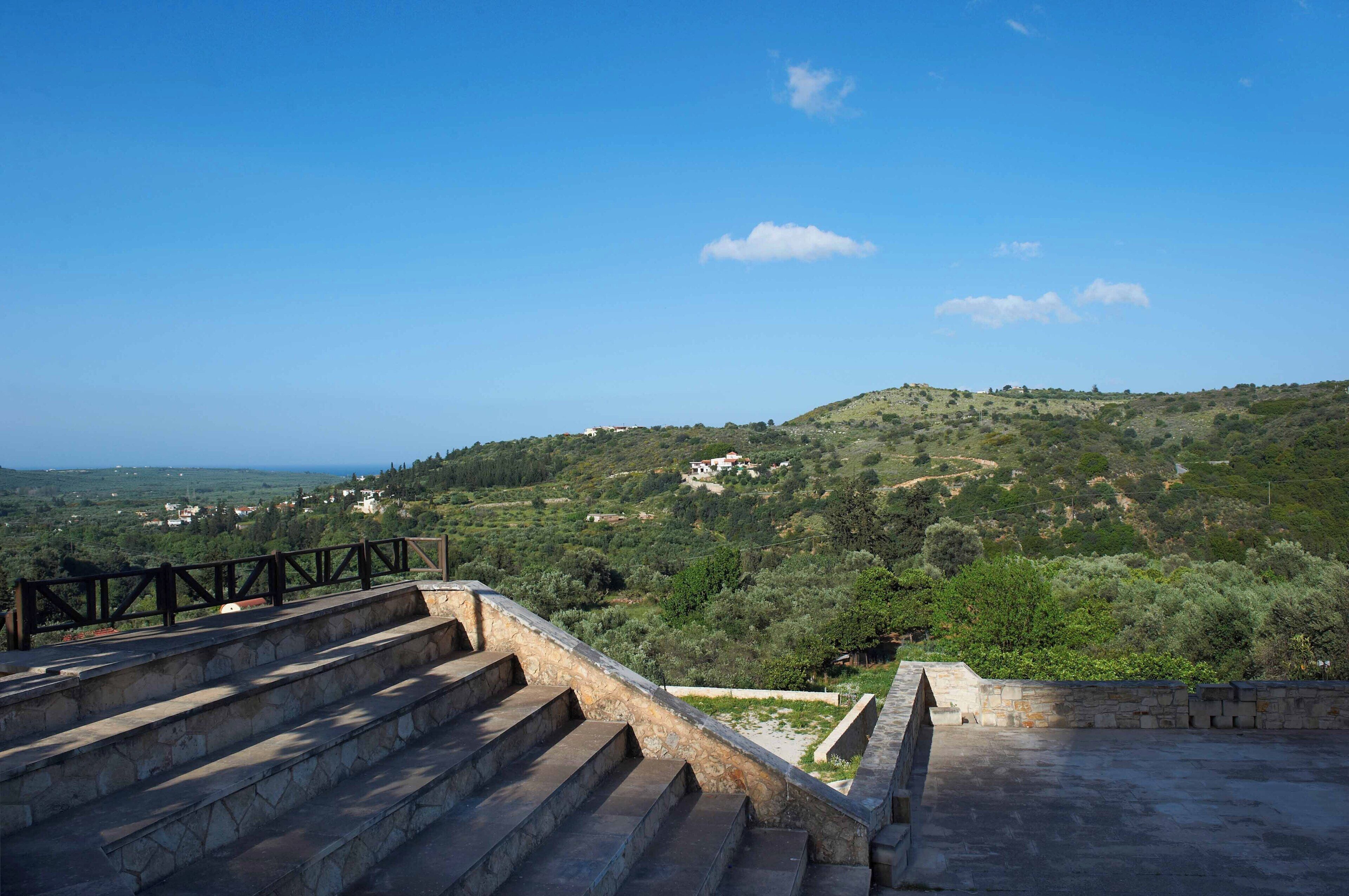 A stone staircase leading to a terrace with a view of a hilly landscape.