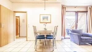 Een kamer met een eettafel en stoelen, een bank, een kamerplant en uitzicht door een glazen deur.