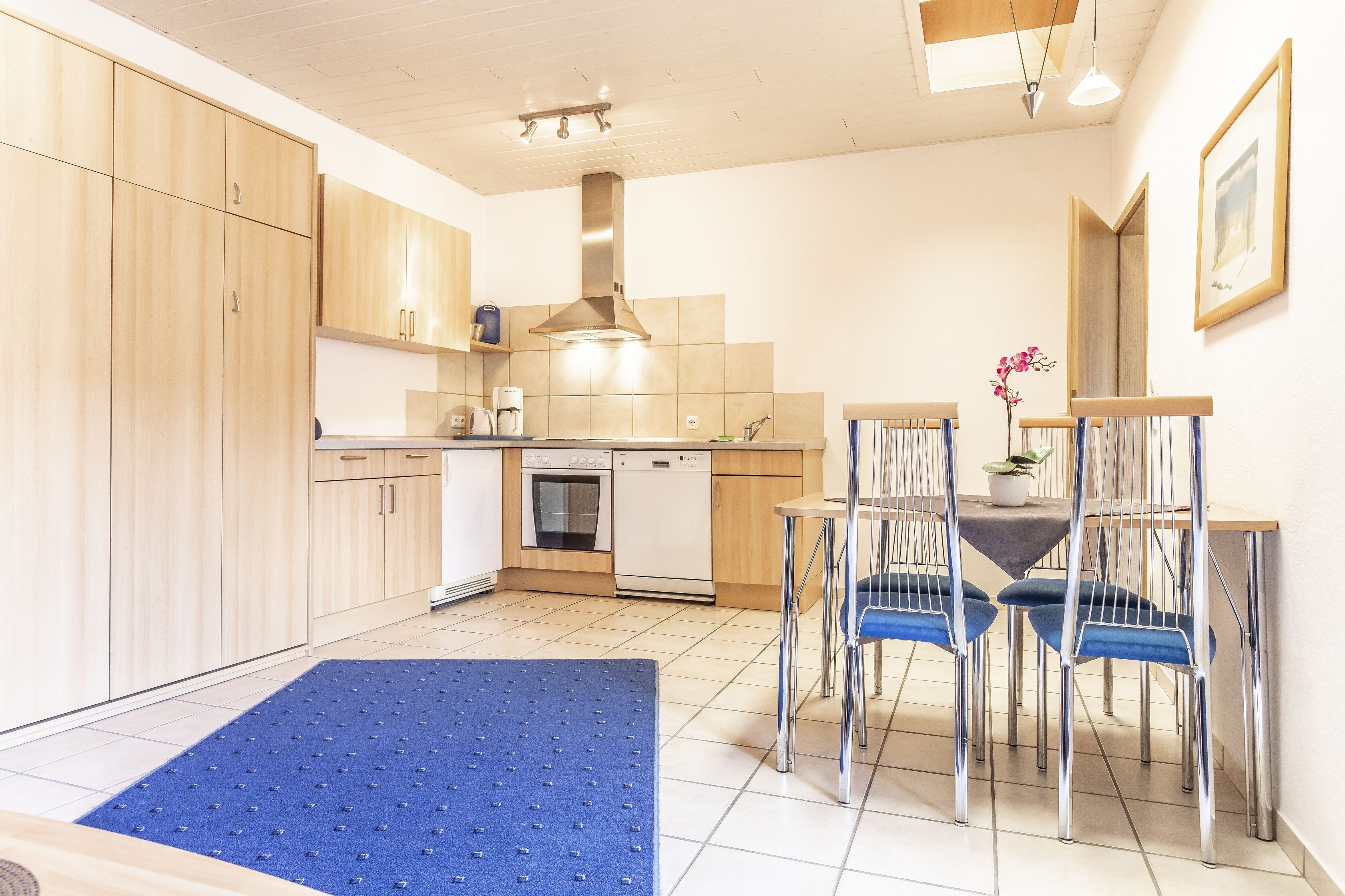 A modern kitchen with wooden cabinets, a built-in oven, and a dining area with blue chairs.