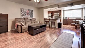 A living room with a sofa, a TV stand, a ceiling fan, and a kitchen area with a microwave and chairs. - See the Valley of the Sun, Arizona State University and Tempe just a short walk. (Tempe)