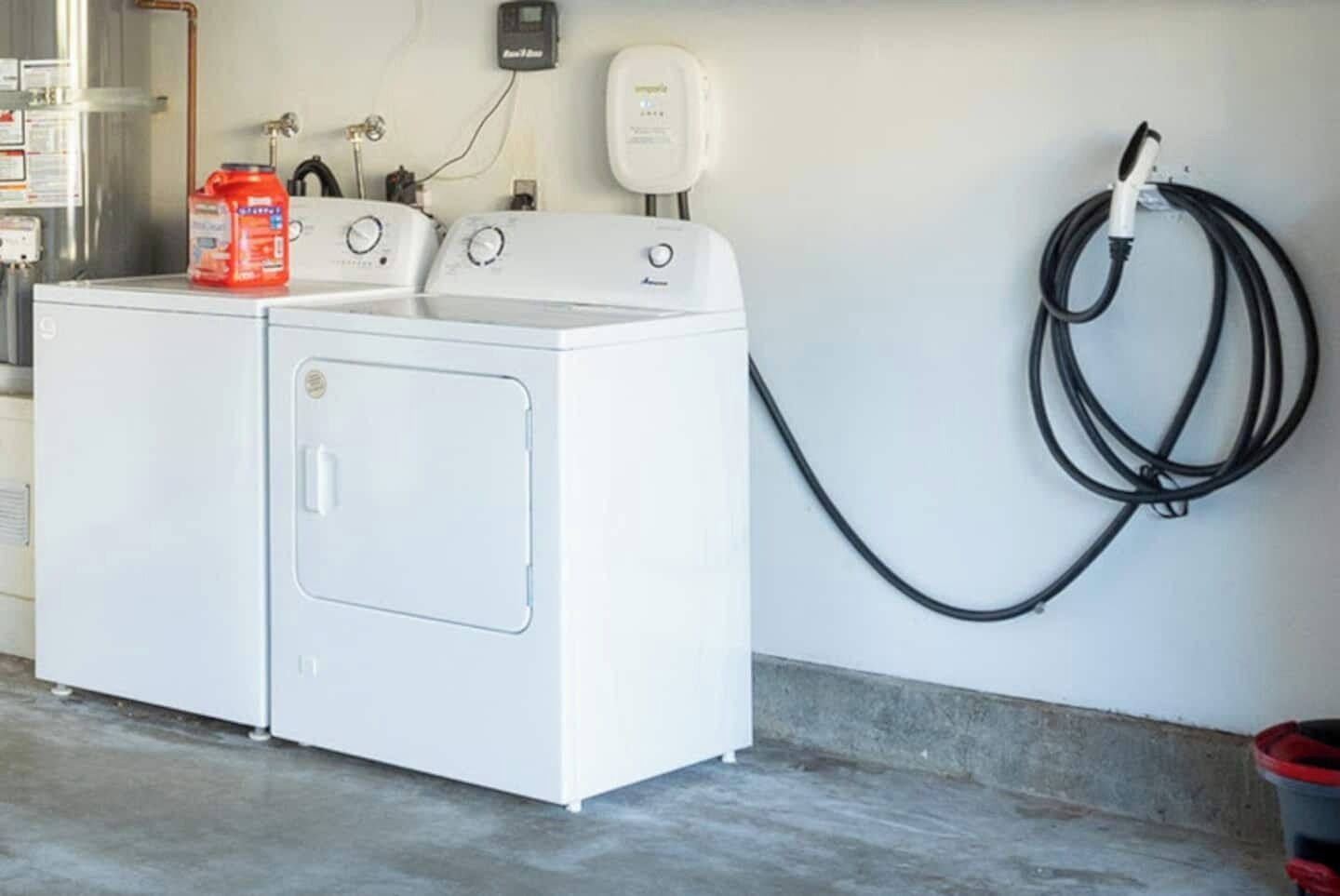A laundry area with a white washer and dryer, a red detergent bottle, and a water hose.