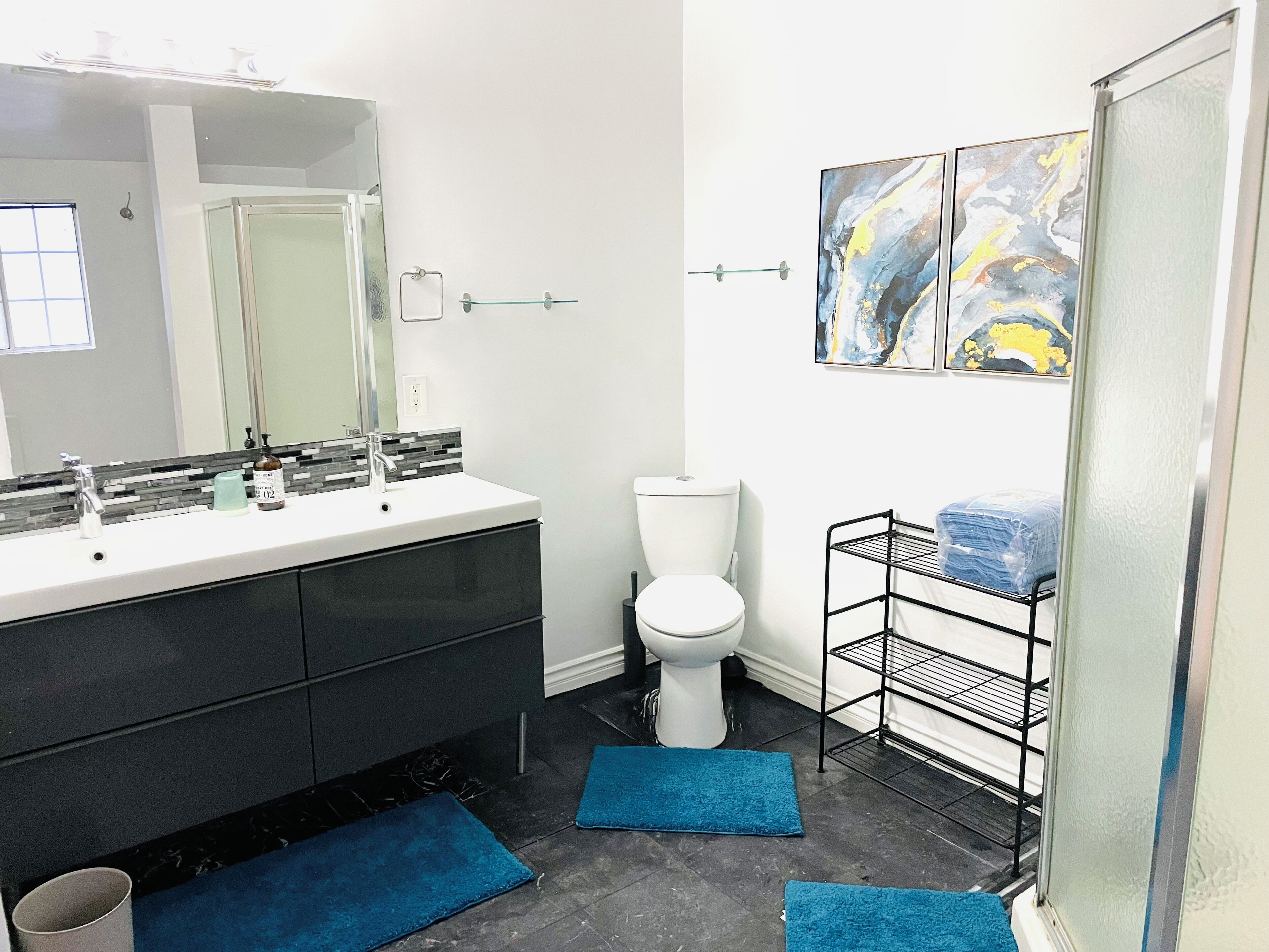 Un bagno con un lavandino bianco, mobili neri, un water bianco e tappeti blu sul pavimento.