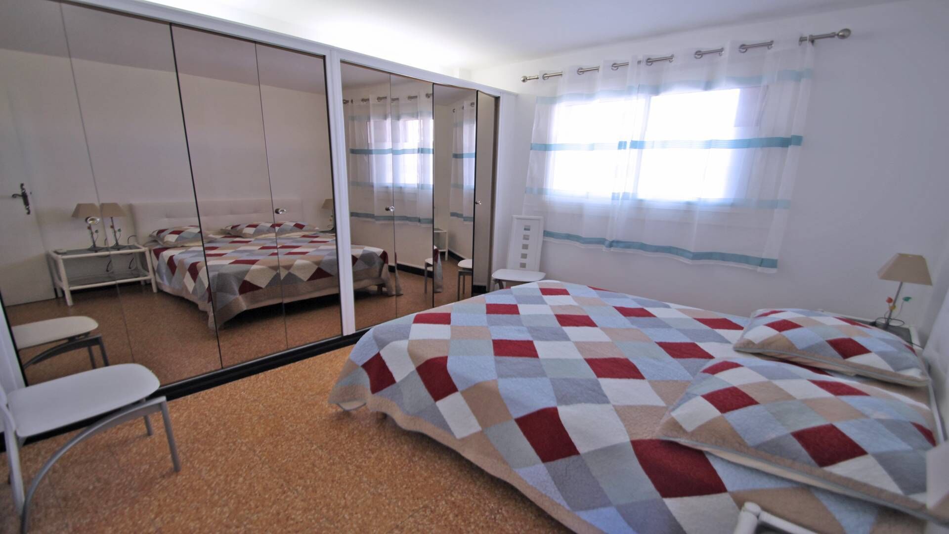 A hotel room with a large bed, a desk, a chair, a wardrobe, and a mirror.