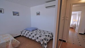 Une petite pièce simple, avec un lit, une chaise et une porte donnant sur une autre pièce.