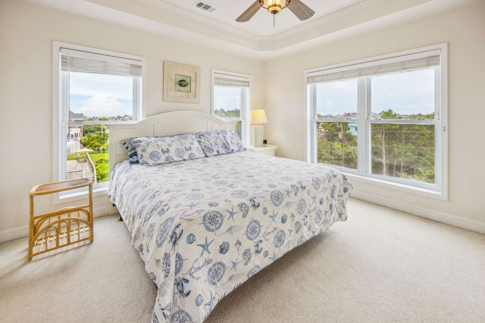 A bedroom with a large bed, two windows, a ceiling fan, and a view of the outdoors.