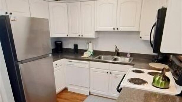 Una cocina con armarios blancos, un refrigerador de acero inoxidable, lavavajillas, estufa y encimera de granito.