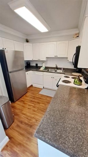 A kitchen with white cabinets, a stainless steel refrigerator, a dishwasher, a stove, and a granite countertop.