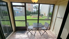 Una habitación soleada con un ventanal de vidrio que da a un patio con una mesa y sillas.