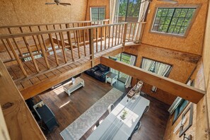 Un vaste espace de vie de style loft, doté d’un plafond haut, d’un escalier en bois et d’un coin repas avec une longue table.
