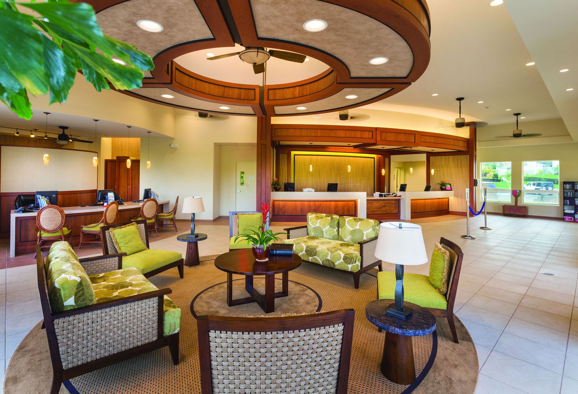 Eine großzügige Lobby mit einer Rezeption, einer Sitzecke mit Sesseln und Sofas sowie einem Deckenventilator.