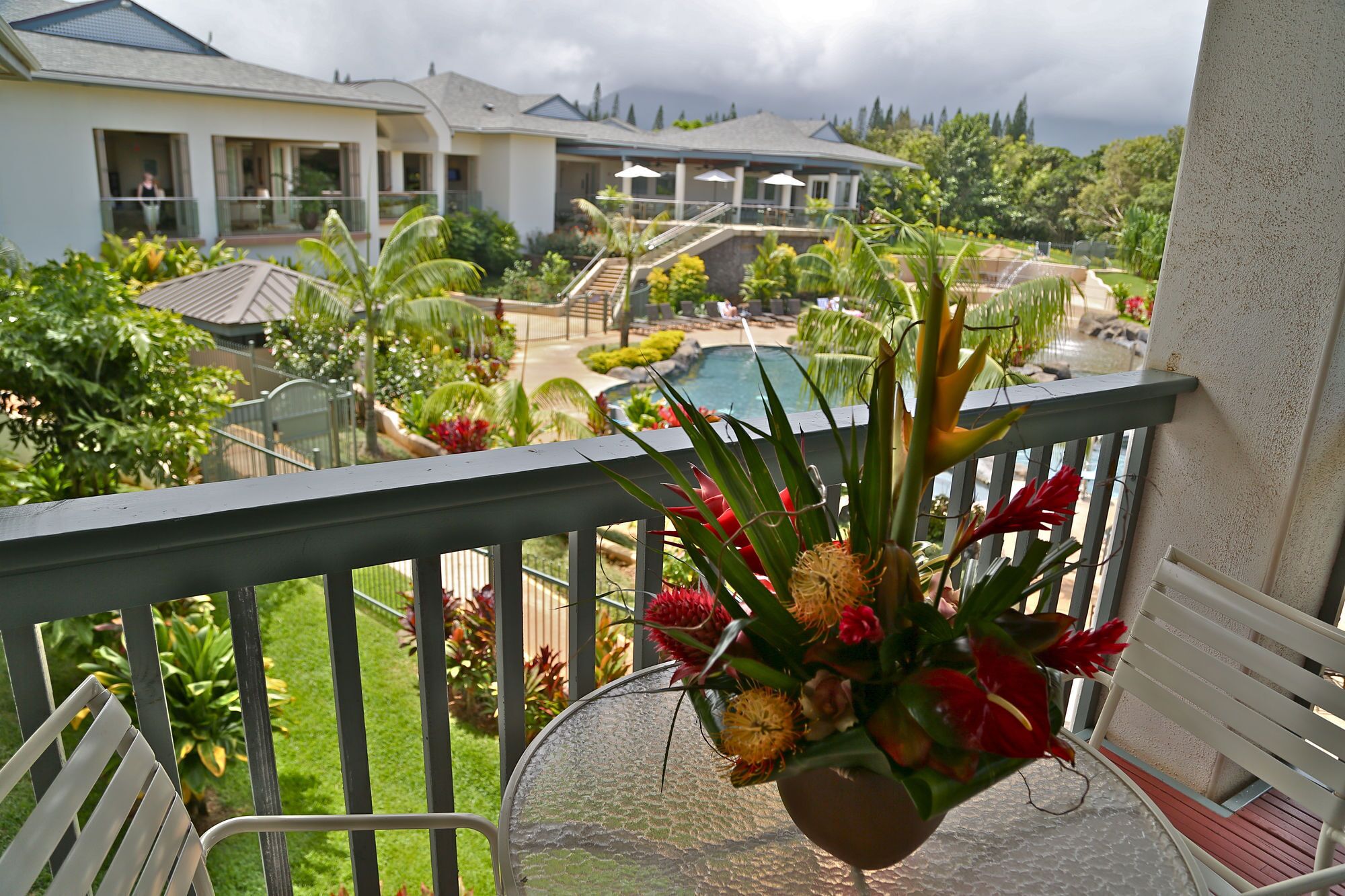 A balcony with a view of a pool, lush greenery, and a building with multiple windows.