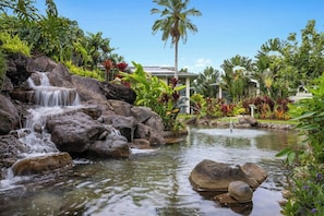 Cascada rodeada de vegetación tropical y una piscina.