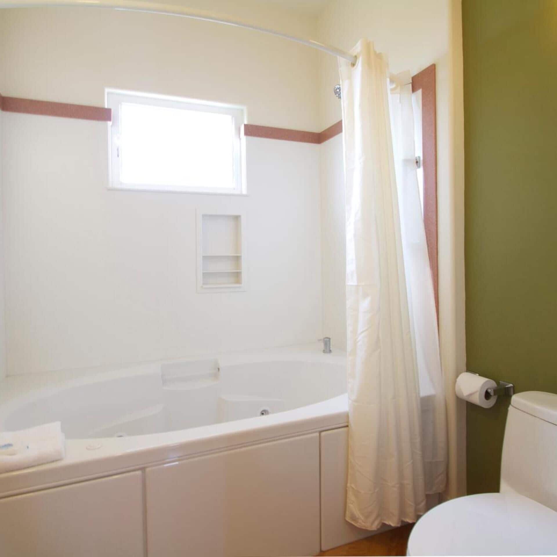 Un baño con bañera, inodoro, ventana y cortina de ducha.