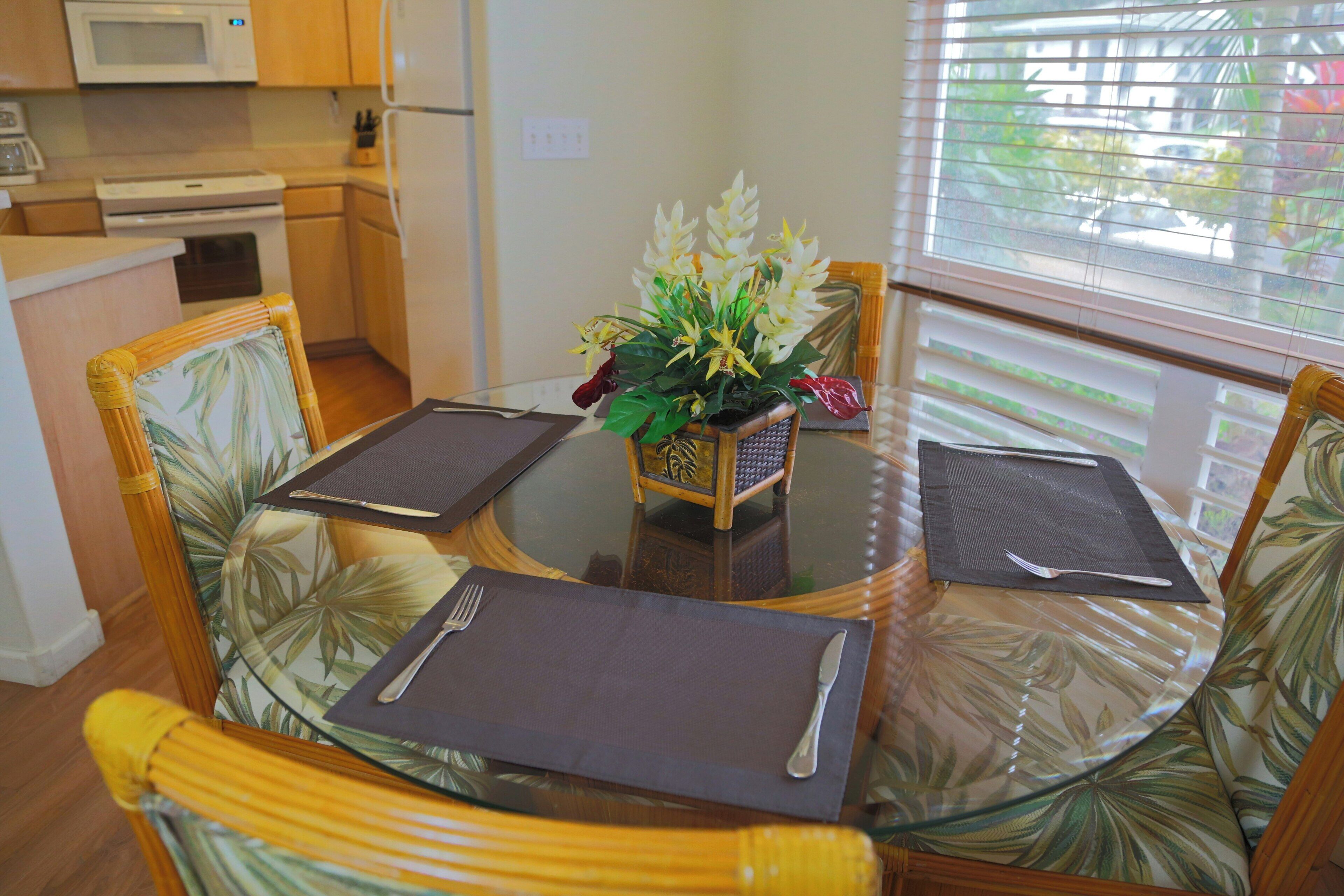 Un comedor con mesa de vidrio, cuatro sillas y un centro de mesa decorativo con planta.