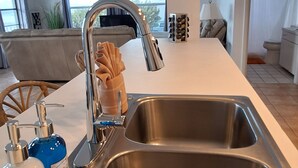 A modern kitchen with a stainless steel sink, a ceiling fan, and a view of the city through large windows.