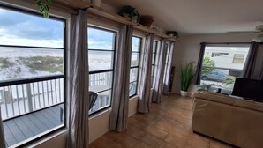 A balcony with large windows overlooking a beach, a beige sofa, and potted plants.