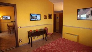 Een hotelkamer met een bed, een bureau met stoel, een televisie aan de muur en een deur naar een andere kamer.