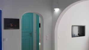 A hallway with a teal door, a painting on the left, and a small window on the right.