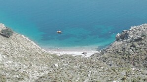 A coastal landscape with a boat on the water, rocky terrain, and a clear view of the sea.
