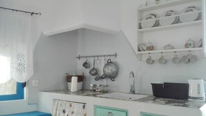 A kitchen with a sink, a stove, and a shelf with dishes.