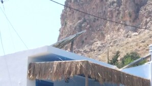 A building with a blue and white facade, a thatched roof, and a rocky hillside in the background.