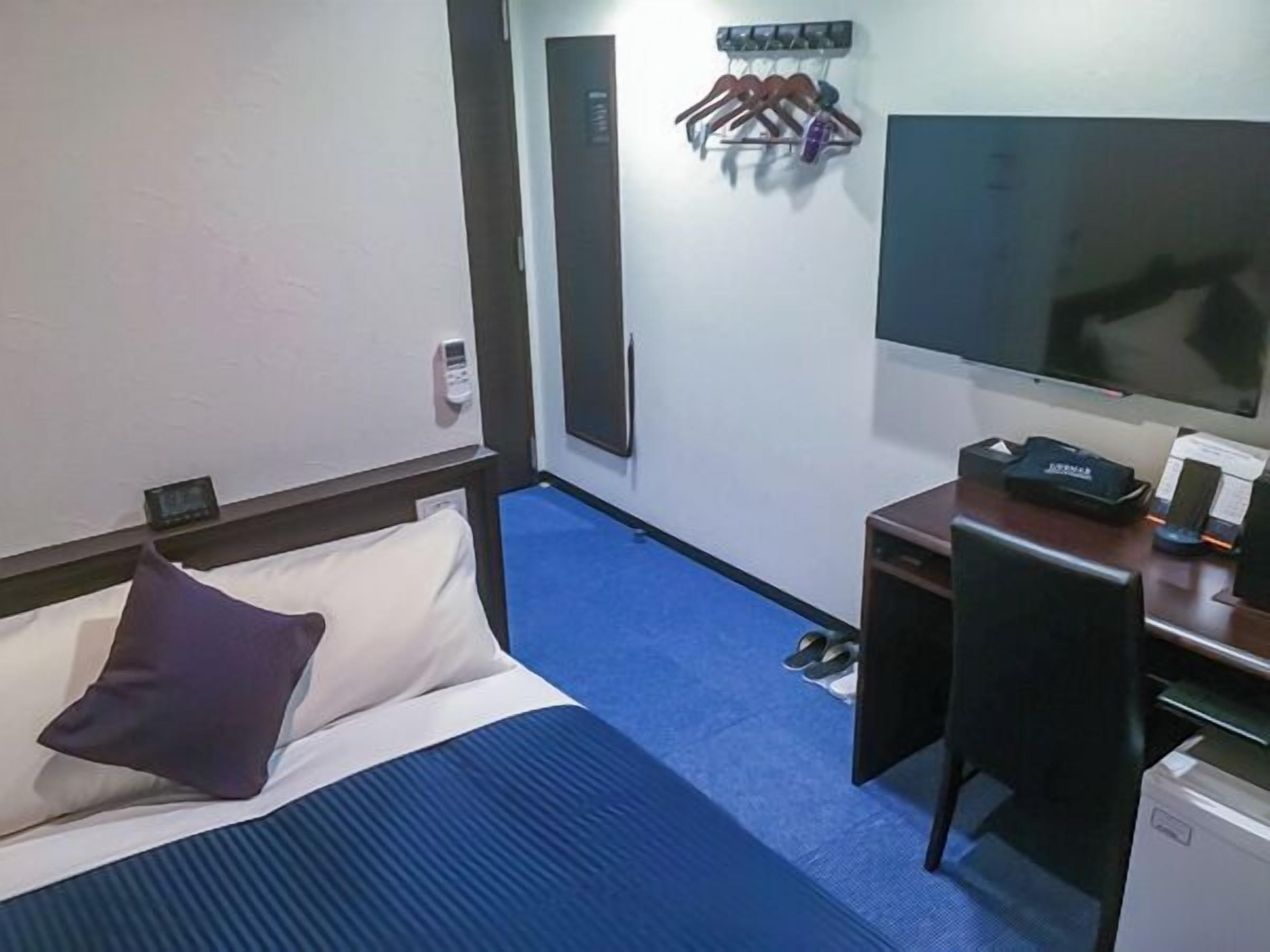 Une chambre d’hôtel équipée d’un lit, d’un bureau, d’une chaise, d’une télévision et d’un porte-manteau avec des cintres.