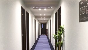 A long, narrow hallway with doors on both sides, a blue carpet, and a potted plant on the right. - HOTEL LiVEMAX Yokkaichi-Ekimae (Yokkaichi)