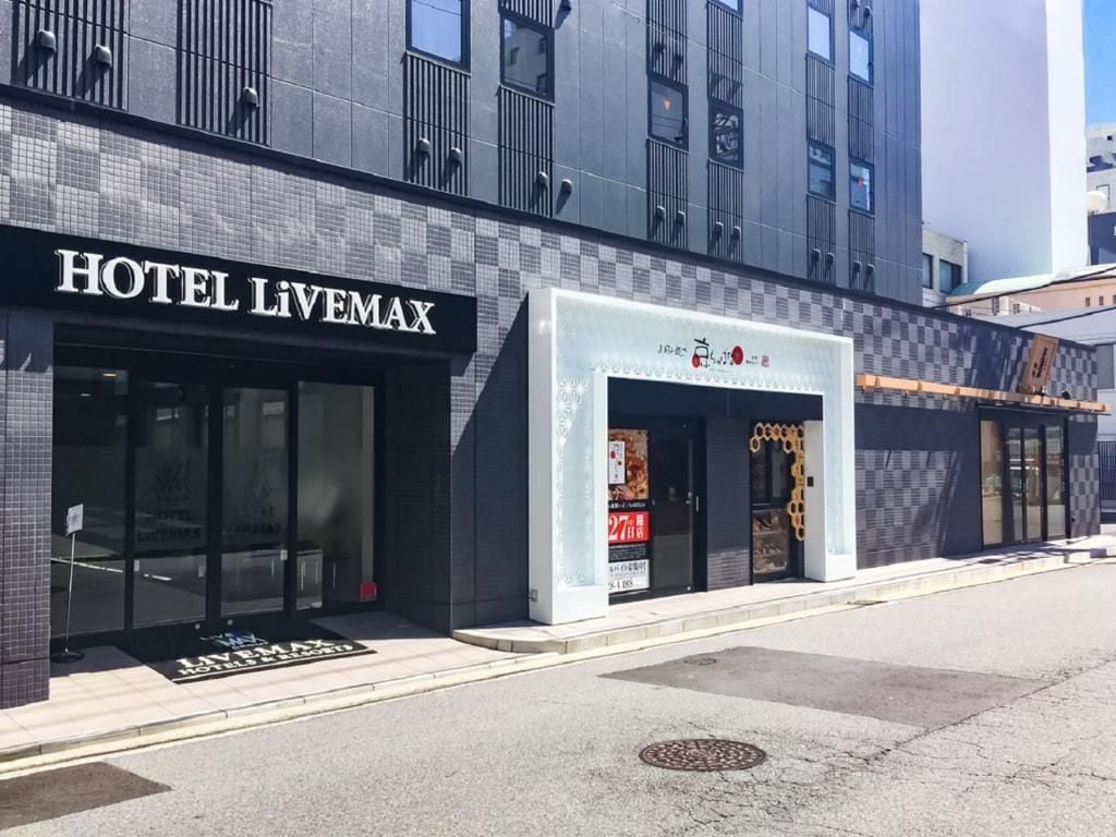 Entrada moderna de hotel com fachada xadrez e uma placa com a inscrição 'HOTEL LIVEMAX'.
