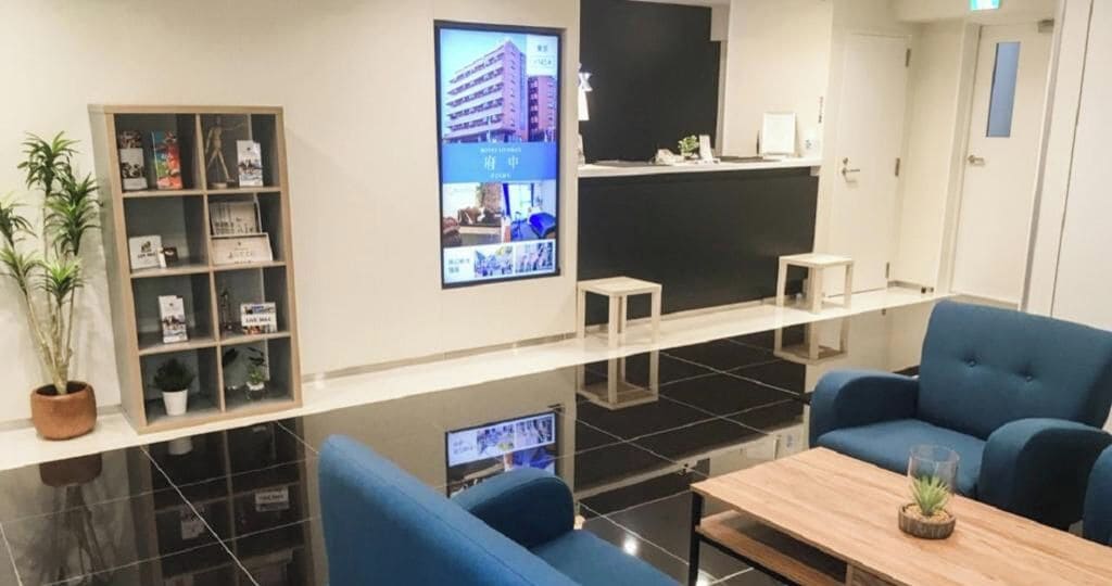 Eine moderne Hotelhalle mit einer Rezeption, einer Lounge und einem digitalen Bildschirm.