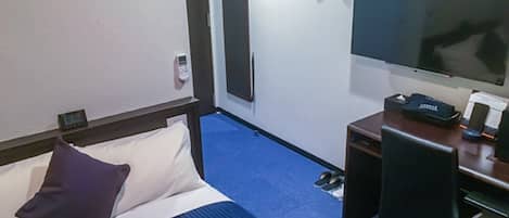 A hotel room with a bed, a desk, a chair, a TV, and a coat rack with hangers.