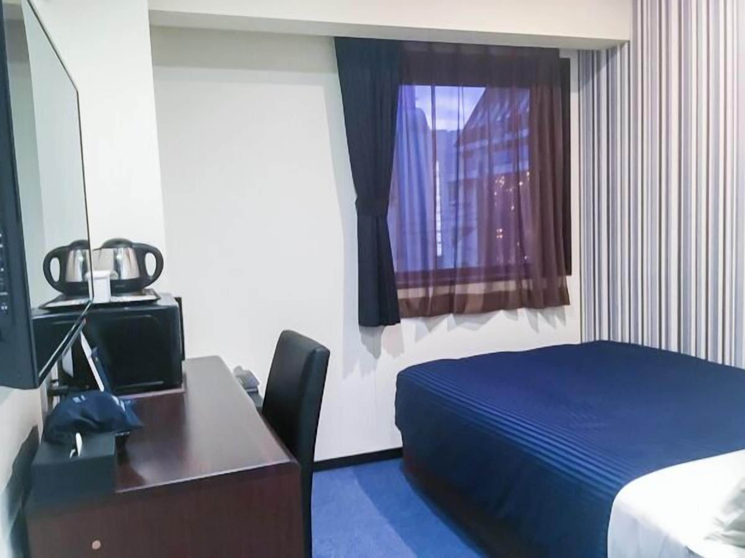 Une chambre d’hôtel avec un lit, un bureau, une chaise, une télévision et une fenêtre avec des rideaux.