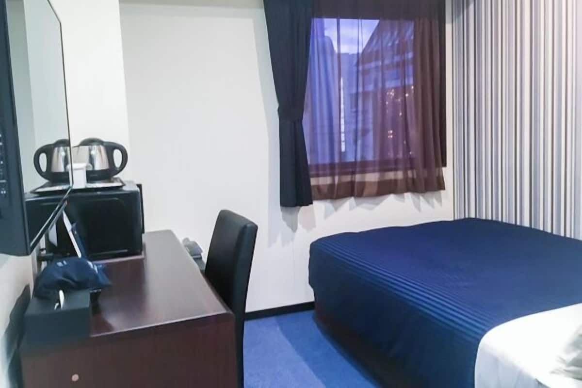Hotelkamer met een bed, een bureau, een stoel, een televisie en een raam met gordijnen.