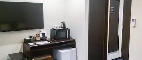 Habitación de hotel con escritorio, refrigerador pequeño, microondas, televisor, silla y cama.