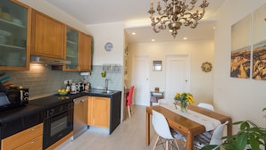 A modern kitchen with wooden cabinets, a black countertop, and a stainless steel sink. There is a dining area with a wooden table and chairs, and a chandelier above. - New picturesque and central penthouse, with a splendid view of the mountains (Torino)