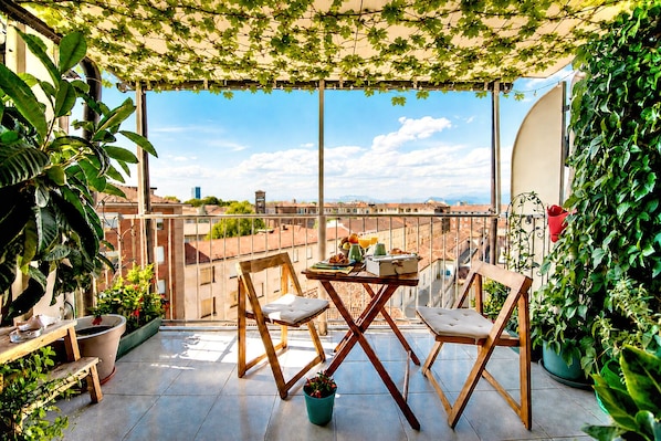 A balcony with a table and chairs, potted plants, and a view of the cityscape.