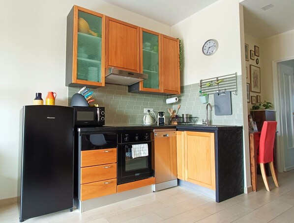 A modern kitchen with wooden cabinets, a black refrigerator, a microwave, an oven, and a sink.
