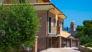 A two-story building with a balcony, a stone wall, and a clear blue sky.
