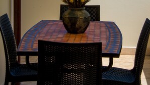 A table with chairs and a vase of flowers on a balcony overlooking the sea and a bell tower.