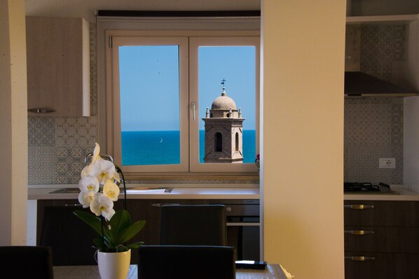 A kitchen with a view of the sea and a bell tower.