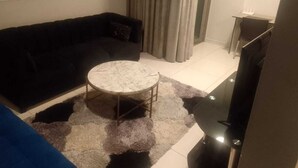 A living room with a black sofa, a round coffee table, a TV stand, and a curtain. - Art Deco Budget Accommodation Rosebank - Hostel (Johannesburg)