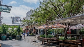 An outdoor café area with wooden benches and umbrellas, surrounded by potted plants and trees. - Art Deco Budget Accommodation Rosebank - Hostel (Johannesburg)