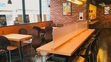 Un café moderno con mesas y sillas de madera, una pared de ladrillo con un menú y ventanas amplias.